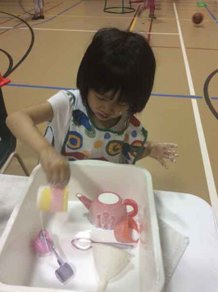 girl playing with a tea set in a water bin